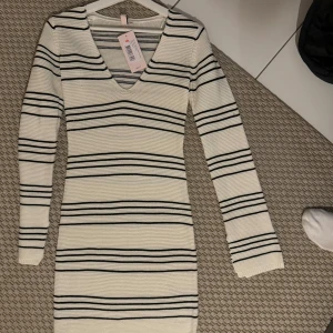 Randig klänning från Nelly - Oanvänd randig klänning från Nelly i storlek XS. Den är vit med svarta ränder och har en v-ringad hals. 