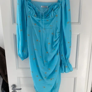 Blå klänning med blommönster från ADOORE - Säljer en superfin blå klänning från ADOORE med små gula blommor. Den har långa ärmar och en snygg rynkad detalj på sidan som ger en cool look. Perfekt för vår och sommar! 💙 Liten i stl! 