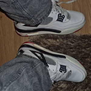 Jordan 4 - Snygga vita sneakers med svarta och röda detaljer. De har en cool design med snörning och en bekväm passform. Perfekta för vardagsbruk eller en avslappnad stil.
