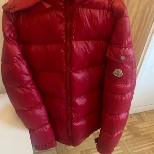 Röd dunjacka från Moncler - Säljer en snygg röd dunjacka från Moncler i mycket bra skick. Jackan har en quiltad design med dragkedja och en praktisk huva. Perfekt för kalla vinterdagar och håller dig varm och stilren. Passar både till vardags och mer uppklädda tillfällen. 🧥🔥