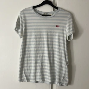 Randig t-shirt från Levi's - Säljer en randig t-shirt från Levi's i ljusblått och vitt. Den är i storlek S till kvinna egentligen, men passar killar också. T-shirten är i bra skick och gjord av mjukt bomullsmaterial. Säljs pågrund av ingen användning.