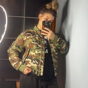 Camouflage bomberjacka från Junkyard - Säljer en snygg camouflage bomberjacka från Junkyard i storlek S. Jackan har en klassisk bomberstil med dragkedja och orange foder. Perfekt för höst och vår, och ger en cool look till vilken outfit som helst. Använd ett fåtal gånger, så den är i mycket bra skick. Passar perfekt för en casual dag ute eller en chill kväll med vänner.