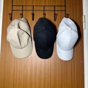 Tre kepsar i olika färger - Tre stilrena kepsar i beige, svart och vit. Oanvända Perfekta för alla säsonger och tillfällen. Kepsarna har en klassisk design med justerbar passform och är tillverkade i ett bekvämt material. Passar både till vardags och träning.