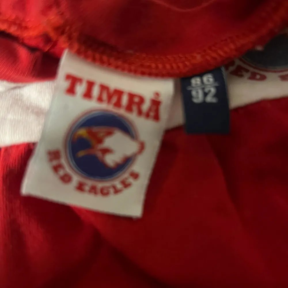 Säljer en superfin röd tröja från Timrå Red Eagles för barn. Tröjan har vita detaljer och ett tryck med Timrås logga på bröstet. Perfekt för små fans som vill visa sitt stöd! Tröjan är i bra skick och redo för nya äventyr. Storlek 86/92. Tröjor & Koftor.