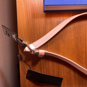 J Lindeberg western leather lizard belt - Säljer ett stilrent vitt bälte från J.Lindeberg i nytt skick. Bältet har en elegant textur och en silverfärgad spänne. Perfekt för både vardag och fest. Längden är 90 cm, vilket motsvarar storlek 32-33 tum. Passar perfekt till jeans eller kostymbyxor. Nypris 1400