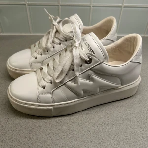Vita sneakers från Zadig & Voltaire - Säljer ett par snygga vita sneakers från Zadig & Voltaire utan synliga defekter, köpta i augusti och är väldigt sparsamt använda. De har en cool design med snörning och en bekväm sula. Skorna kommer i originalkartong med dustbag. Original priset är 3600, men jag säljer dom för 1500 vid snabb affär. Budgivning om fler är intresserade. Hör av dig om du vill ha fler bilder! 💗(kan mötas i Stockholm)