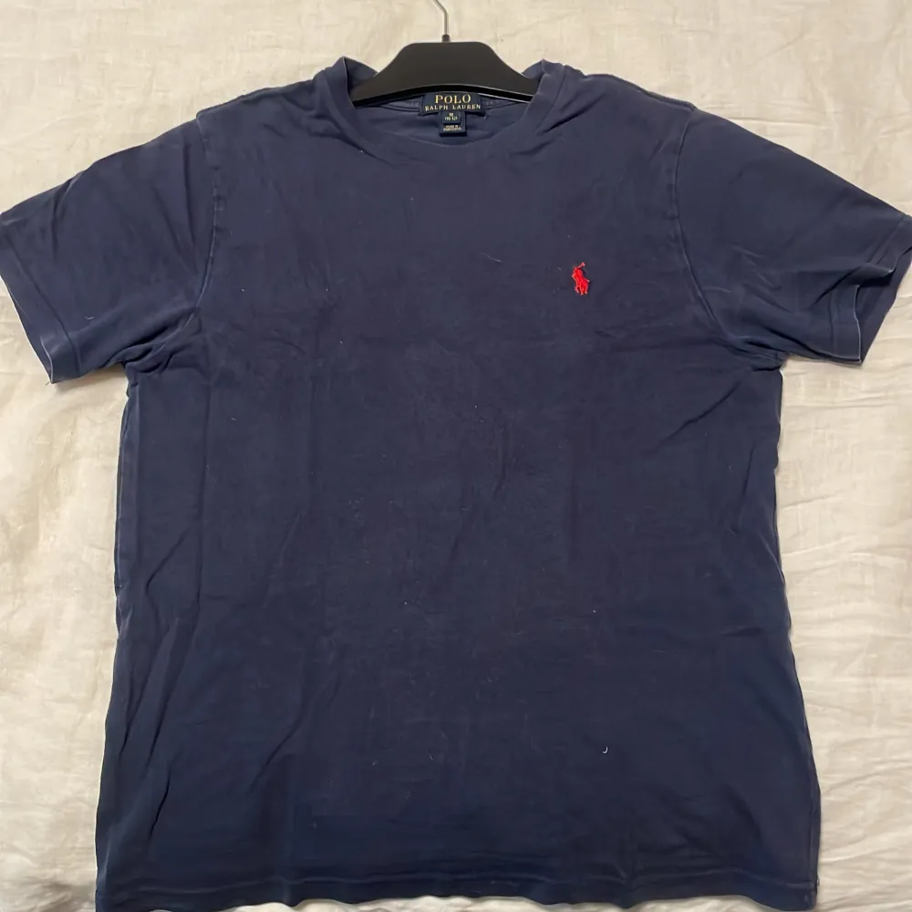 Säljer en klassisk mörkblå t-shirt från Polo Ralph Lauren i storlek M dock för åldrar 10-12. Den har en röd broderad logga på bröstet och är gjord av mjuk bomull. Perfekt för en avslappnad stil eller sommarens äventyr. Passar till allt!. T-shirts.