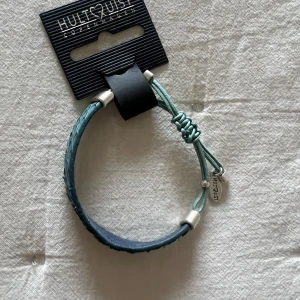 Turkost armband från Hultquist - Snyggt turkost armband från Hultquist med flätad design och justerbar knut. Perfekt för att ge en färgklick till din outfit. Armbandet har silverfärgade detaljer och en liten berlock med märkets namn. Passar både till vardags och fest! Helt nytt!!