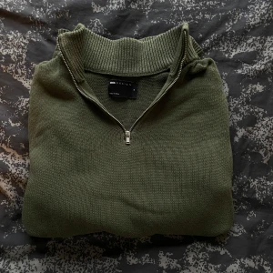 Olivgrön stickad tröja från ASOS DESIGN - Säljer en snygg olivgrön stickad tröja från ASOS DESIGN. Den har en dragkedja vid halsen och ribbade detaljer vid krage och ärmslut. Perfekt för kyliga dagar och passar både till vardags och lite mer uppklädda tillfällen. Superbekväm och stilren! 🍃