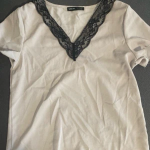 Vit topp med spetsdetalj från Shein - Säljer en söt vit topp från Shein i storlek XS. Den har en v-ringad design med svart spetsdetalj som ger en elegant touch. Perfekt för både vardag och festliga tillfällen. Toppen är kortärmad och i bra skick! Om du är intresserad eller har några funderingar är du välkommen att höra av dig!💕💕 (kommer ej prova på o skicka bild) 