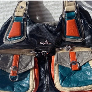 Jätte fin väska från Angel Kiss - Säljer en unik och färgglad axelväska från Angel Kiss. Den är köpt i Berlin men behöver nytt hem. Är i jätte fint skick. Den har flera fickor med dragkedjor och dekorativa detaljer. Perfekt för att liva upp vilken outfit som helst! 