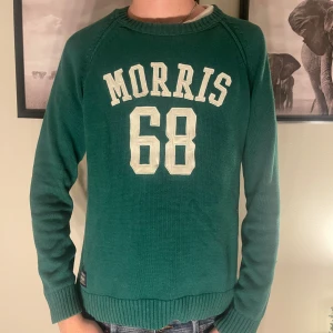 Grön tröja från Morris - Säljer en snygg grön tröja från Morris med texten 'Morris 68' i vitt på framsidan. Tröjan är i bra skick och har långa ärmar med mörka armbågslappar. Perfekt för höst och vår! NYPRIS cirka 1300 kr