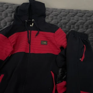 Armani Jeans Dress - Säljer en snygg svart och röd hoodie från Armani Jeans. Den har en dragkedja framtill och en justerbar huva med snören. Tröjan är randig och har en logga på bröstet. Perfekt för en casual look eller träning. Passar bra till höst och vår! Storlek M