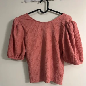 Rosa topp med puffärmar - Säljer en superfin rosa topp med puffärmar. Den har en härlig textur som ger en unik look. Perfekt för både vardag och fest!