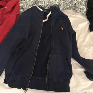 Blå hoodie från Ralph Lauren - Säljer en snygg blå hoodie från Ralph Lauren med dragkedja och klassisk logga på bröstet. Perfekt för en avslappnad stil och passar till alla tillfällen. Den är i bra skick och superbekväm att ha på sig. Perfekt för höst och vår!