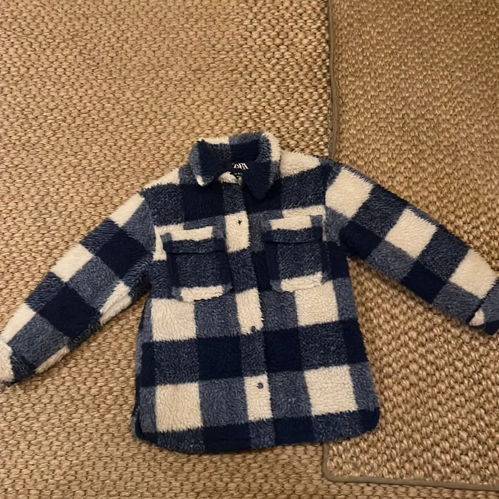 Supermysig rutig teddyjacka från Zara i blått och vitt. Perfekt för höst och vinter med sin fluffiga och varma design. Jackan har långa ärmar och knappar framtill, samt två praktiska bröstfickor. Perfekt för att hålla sig varm och stilren under kyliga dagar! 🧥❄️. Jackor.