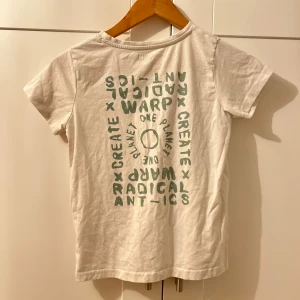 Vit t-shirt med tryck - Säljer en vit t-shirt med grönt tryck på både fram- och baksidan. Texten säger 'One Planet' och 'Create Radical Antics'. Perfekt för en avslappnad stil och gjord i mjukt material. Passar bra till vardags eller chillhäng. Använt något gång köpt längesen.