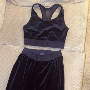 Svart träningsset från Stronger - Snyggt svart velourset från Stronger i storlek S med byxor och topp. Perfekt för träning eller en avslappnad dag hemma. Byxorna har en loose passform och hög midja med strongers logga. 