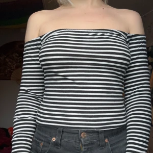 Randig offshoulder topp - Säljer en superfin randig offshoulder topp i svart och vit. Den är tight och har långa ärmar, perfekt för både vardag och fest. Toppen är i bra skick och passar till många olika outfits!