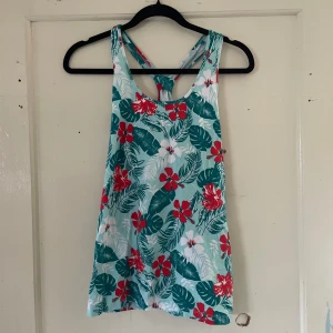 Blommig linne från Esmara - Säljer ett somrigt linne från Esmara med ett färgglatt blommönster. Linnet är ärmlöst och har en härlig mix av gröna blad och röda blommor på en ljus bakgrund. Perfekt för varma sommardagar!