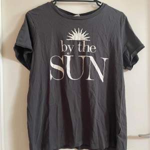 En grå t-shirt med vit tryck där det står ”by the sun”