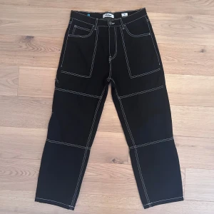 Svarta byxor med kontrastsömmar - Snygga svarta byxor med vita kontrastsömmar och flera fickor fram och bak. Byxorna har en rak passform och är perfekta för en avslappnad stil. De har en knapp och dragkedja framtill.