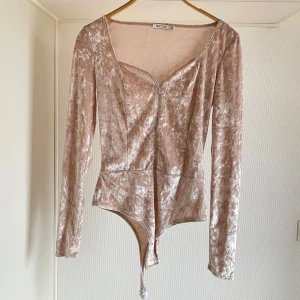 Beige sammetstopp från NLY One oanvänd M - Snygg beige body i sammet från NLY One med långa ärmar och en djup v-ringning. Perfekt för att ge en lyxig touch till din outfit.