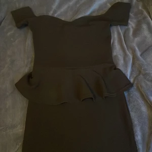 Svart klänning  - Snygg svart klänning med offshoulder-design och volangdetalj i midjan. Perfekt för en stilren look. Klänningen är i storlek S och har en elegant passform.