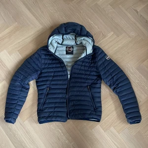 Mörkblå dunjacka från Colmar - Säljer en snygg mörkblå dunjacka från Colmar. Jackan är sparsamt använd och därmed mycket bra skick. ”Hängaren” har lossnat som syns på bild 3 men är nog lätt att laga och inget som märks vid användning. Storlek 48 som motsvarar ungefär S. Hör gärna av er för fler bilder eller funderingar.😇