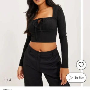 Svart ribbad topp från Nelly - Snygg svart ribbad topp från Nelly med långa ärmar och knytning framtill. Toppen är croppad och har en stilren design som passar perfekt till olika tillfällen.