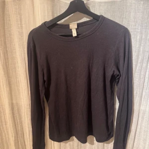 Svart långärmad tröja från H&M - Säljer en enkel och stilren svart långärmad tröja från H&M. Perfekt för lager-på-lager eller att bära som den är. Tröjan har en rund halsringning och är gjord i ett mjukt material för extra komfort.