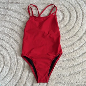 Röd baddräkt från Jolyn - Snygg röd baddräkt från Jolyn med dubbla axelband och öppen rygg. Perfekt för simträning eller en dag på stranden. Tillverkad i 100% polyester för en bekväm passform. Är i nyskick. Nypris 800kr säljs för 200 kr.