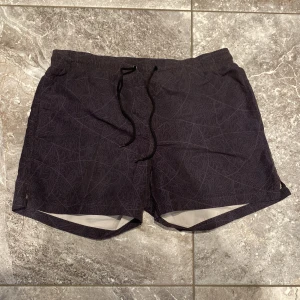 Svarta shorts med mönster - Snygga svarta shorts med diskret mönster och snörning i midjan. Perfekta för en avslappnad stil. De har en elastisk midja och är gjorda i ett lätt material som passar bra för varma dagar.