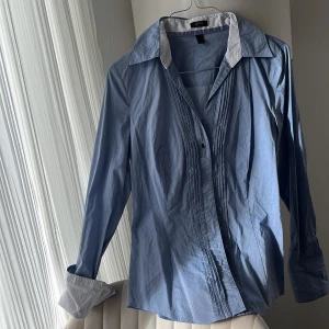 Blå skjorta från Esprit - Snygg blå skjorta från Esprit med vit kontrastkrage och manschetter. Skjortan har långa ärmar och knappar framtill. Perfekt för en stilren look.