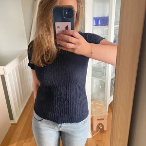 Mörkblå ribbad topp - Säljer en mörkblå ribbad topp med korta ärmar. Toppen har en tight passform och är perfekt för en stilren look. Den är enkel men elegant och passar bra till jeans eller kjol.