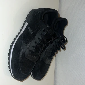 Svarta sneakers från Boss - Snygga svarta sneakers från Boss med snörning och en robust sula. Skorna har en stilren design med Boss-loggan på sidan. Perfekta för en casual look.