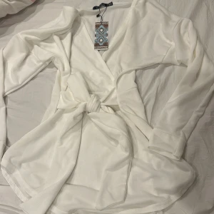 Vit omlottblus med knytband - Säljer en stilren vit omlottblus från boohoo med knytband i midjan. Blusen har långa ärmar och en elegant v-ringning. Perfekt för en chic och avslappnad look.