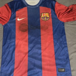 Barcelona tröja 2024 - Snygg fotbollströja från Nike i klassiska blåröda färger med FC Barcelona-emblem på bröstet. Tröjan har korta ärmar och ett randigt mönster. Perfekt för alla Barça-fans som vill visa sitt stöd.