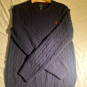 Mörkblå kabelstickad tröja från Ralph Lauren - Säljer en stilren mörkblå kabelstickad tröja från Ralph Lauren. Tröjan är köpt på kidsbrandstore och är storlek XL Barn. Tröjan är nopprig men annars i bra skick. Pris kan diskuteras och skicka frågor vid funderingar