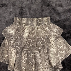 Ormmönstrad kjol från Gina Tricot - Snygg ormmönstrad kjol från Gina Tricot med volanger. Kjolen har en elastisk midja för bekväm passform och är perfekt för att ge en trendig touch till din outfit. 🐍Skulle säga att den passar 36-38