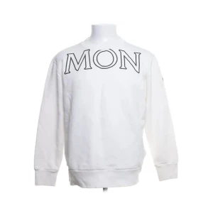 Vit sweatshirt från Moncler - Säljer en stilren vit sweatshirt från Moncler med stora bokstäver på framsidan och baksidan. Tröjan har långa ärmar och en rund halsringning. Perfekt för en avslappnad och trendig look.