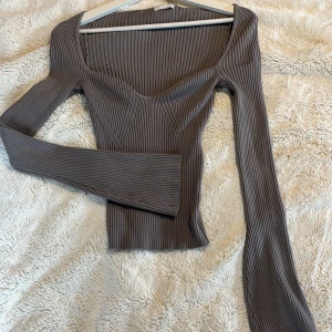 Grå ribbad topp - Snygg grå ribbad topp med lång ärm och fyrkantig halsringning. Perfekt för en stilren look. Armarna är utsvängda! 