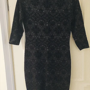 Svart mönstrad vinter klänning från H&M  - Snygg svart klänning med ett subtilt mönster. Den har trekvartsärmar och en figurnära passform som ger en elegant look. Perfekt för både vardag och speciella tillfällen.