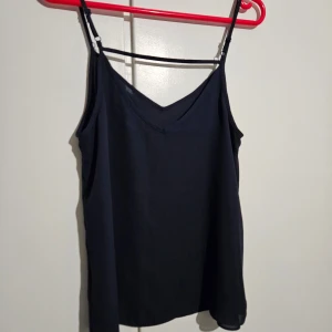 Svart linnetopp med justerbara axelband - Snygg mörkt blå linnetopp med justerbara axelband och v-ringning. Perfekt för varma dagar eller som ett lager under en kavaj. Enkel och stilren design som passar till det mesta.