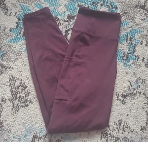 Träningstights - Träningstights från HM i strl S. Vinröda med ficka på höger lår, perfekt för mobilen. Sömmen lite sliten på baksidan annars i bra skick. Hög midja som inte glider ner och går ner till fotlederna. Säljer matchande sportbh från ICIW också :) båda tillsammans för 140kr