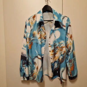 Mönstrad skjorta i blå och bruna toner - Snygg skjorta med abstrakt mönster i blå, vit och brun. Skjortan har långa ärmar och knappar framtill. Perfekt för en unik och stilren look.