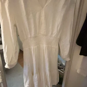 Vit klänning med v-ringning - Säljer en söt vit klänning med v-ringning och långa ärmar från Zara. Klänningen har en smockdetalj i midjan som ger en fin passform. Perfekt för vår och sommar!