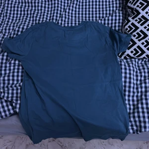 Blå t-shirt med broderad logga - Säljer en stilren blå t-shirt från Lyle & Scott med en liten broderad logga på bröstet. Perfekt för en avslappnad look.