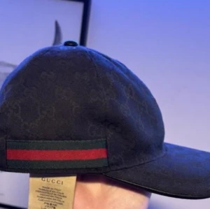 Svart keps från Gucci - Snygg svart keps från Gucci med diskret mönster och klassiska röd-gröna ränder på sidan. Perfekt för en stilren look.