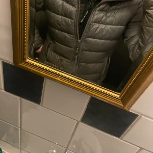 Grön dunjacka från Uhip - Säljer en stilren grön dunjacka från Uhip. Jackan har en dragkedja framtill och två praktiska fickor med dragkedjor. Perfekt för tidiga vår dagar med sin quiltade design och höga krage. Ett hål vid armen se på bild 5. Och ett till hål på andra armen (inte lika stort) kom privat för bild